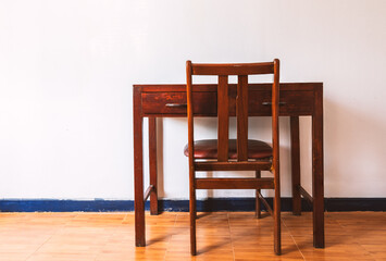 Beautiful vintage wooden table and chair, back side view of the table and chair, table and chair in white room wall and brown floor, no people, natural light with warm tone.