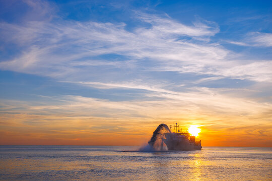 Vessel engaged in dredging at sunset time. Hopper dredger working at sea. Ship excavating material from a water environment. Beautiful sunset, Baltic sea