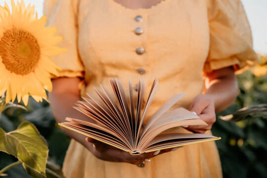 Woman flips through pages of old paper book on sunflowers field background. Aesthetics scene. Education, science, nature concept.
