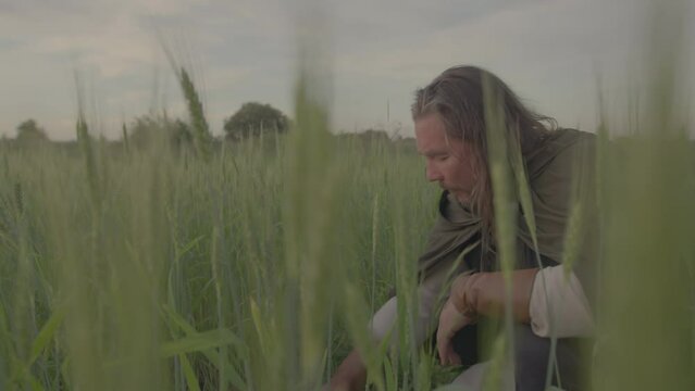 A white Caucasian man in medieval clothes eats in a wheat field and prays to God