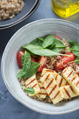 Grey plate with quinoa, grilled haloumi, fresh spinach and tomato salad, vertical shot, close-up