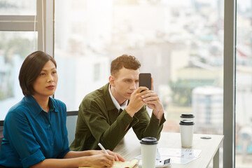Young man taking photos of important information on smartphone during conference