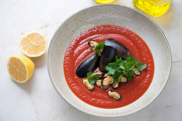 Plate of tomato soup with mussels and fresh parsley on a light-beige marble background, horizontal shot, selective focus