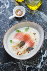 Bowl of cold melon soup served with jamon, vertical shot on a black marble background, elevated view