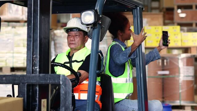 black woman selfie. Warehouse asian male worker staff driving forklift operator moving boxes in industrial container warehouse factory. Asian senior Man worker woking with forklift.