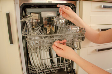 Woman's hand close-up with a transparent glass goblet. A woman puts dishes in the dishwasher or takes it out of it.