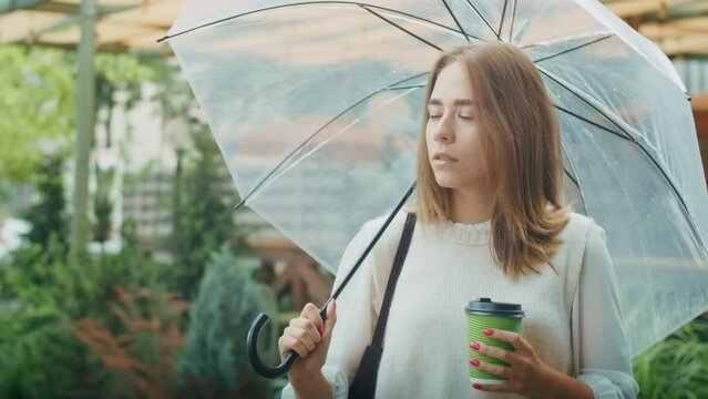 joyful girl drinks tea on the street in rainy weather, and speaks on the phone.