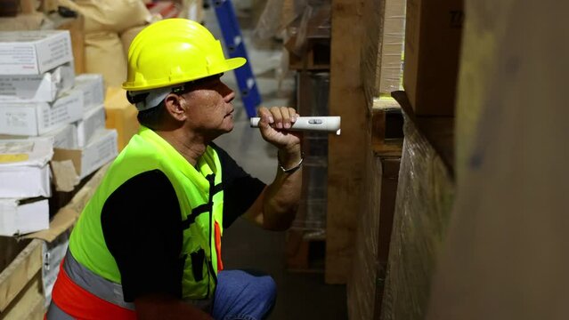 Security guard working at night. Senior asian male security working with flashlight at larg warehouse factory.