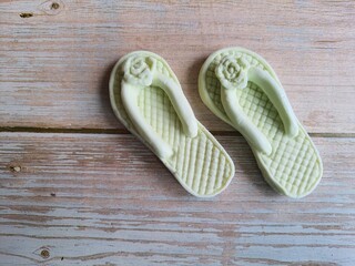 Pair of white beach slippers made from soap, miniature bathing sandal display. Crafts, extra income. Isolated on a wooden table, top view with text space.