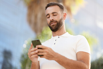 Fototapeta premium Confident handsome latin man using mobile app shopping online on the street. Bearded businessman holding smartphone checking email, searching information. Modern technology, e-commerce concept