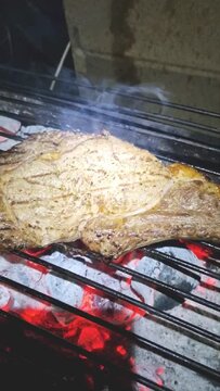 Chulet&oacute;n humeante sobre la parrilla y las brasa de una barbacoa