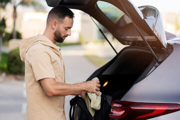 Handsome latin man loading bag in car trunk. Driver planning road trip, transportation concept 