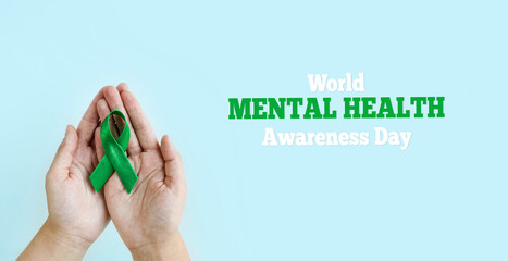 World Mental health awareness day. Woman hands holding green ribbon on blue background.