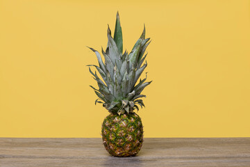Pineapple on a wooden table with a yellow background, whole.