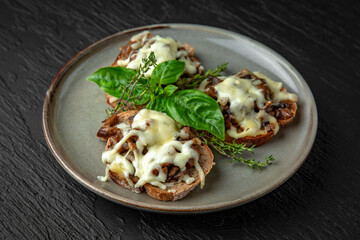 Healthy nutritious breakfast of bruschetta with fried forest mushrooms, cheese, basil and thyme in a ceramic plate on a dark textured background. Restaurant menu Isolated on black
