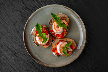 Healthy nutritious breakfast of bruschetta with tomatoes, shrimp and basil in a ceramic plate on a dark textured background. Restaurant menu Isolated on black