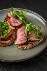 Healthy nutritious breakfast of bruschetta with pastrami beef ham and herbs in a ceramic plate on a dark textured background. Restaurant menu Isolated on black