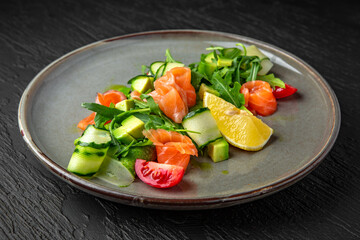 Salad of salmon, avocado, tomatoes, herbs and nuts in a ceramic plate on a dark textured background. Restaurant menu Isolated on black