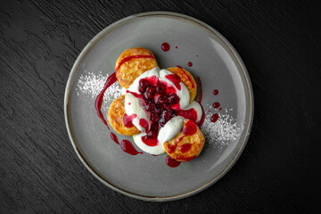 Cottage cheese pancakes with berry jam and sour cream. Healthy hearty breakfast in a ceramic plate on a dark textured background. Restaurant menu Isolated on black