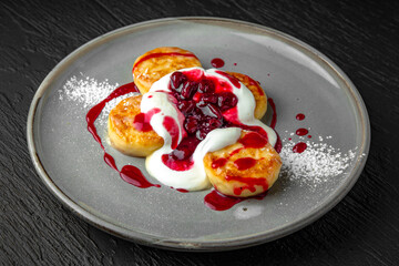 Cottage cheese pancakes with berry jam and sour cream. Healthy hearty breakfast in a ceramic plate on a dark textured background. Restaurant menu Isolated on black