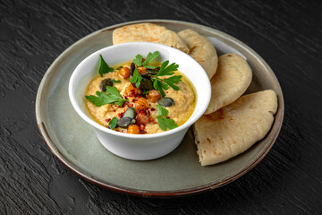 Hummus in a ceramic plate on a dark textured background. Restaurant menu Isolated on black
