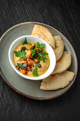 Hummus in a ceramic plate on a dark textured background. Restaurant menu Isolated on black