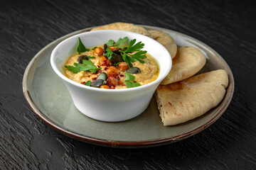 Hummus in a ceramic plate on a dark textured background. Restaurant menu Isolated on black