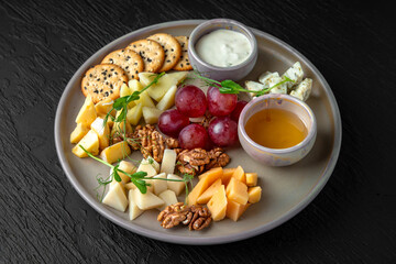 Cheese plateau. Appetizer of parmesan, camembert, dorblu, cheddar, grapes and other fruits in a ceramic plate on a dark textured background. Restaurant menu Isolated on black
