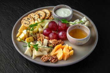 Cheese plateau. Appetizer of parmesan, camembert, dorblu, cheddar, grapes and other fruits in a ceramic plate on a dark textured background. Restaurant menu Isolated on black