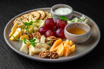 Cheese plateau. Appetizer of parmesan, camembert, dorblu, cheddar, grapes and other fruits in a ceramic plate on a dark textured background. Restaurant menu Isolated on black
