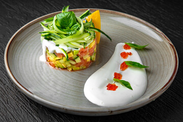 Tartar with salmon and avocado in a ceramic plate on a dark textured background. Restaurant menu Isolated on black