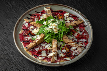 Veal carpaccio in a ceramic plate on a dark textured background. Restaurant menu Isolated on black