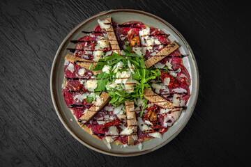 Veal carpaccio in a ceramic plate on a dark textured background. Restaurant menu Isolated on black