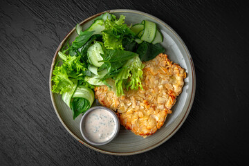 Chicken schnitzel in almond flakes in a ceramic plate on a dark textured background. Restaurant menu Isolated on black