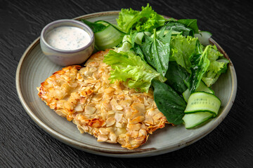 Chicken schnitzel in almond flakes in a ceramic plate on a dark textured background. Restaurant menu Isolated on black