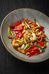 Thai chicken pasta in a ceramic plate on a dark textured background. Restaurant menu Isolated on black