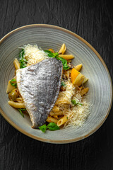 Penne pasta with dorado and parmesan in a ceramic plate on a dark textured background. Restaurant menu Isolated on black