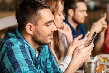 technology, lifestyle and people concept - group of friends with smartphones at restaurant