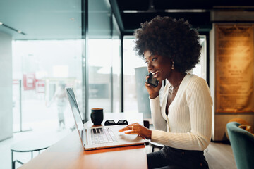 Obraz premium Smiling young african woman sitting with laptop in cafe