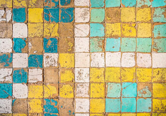 Background of small square old tiles of different colors in poor condition with cracks, scuffs and...
