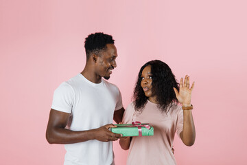 Happy african man giving gifts to his girlfriend, pink studio background, free space. Loving...