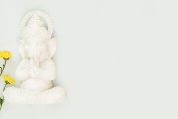 Sculpture of Lord Ganesha with flowers on a light blue background with copy space. Holiday of Ganesh Chaturthi. Ganesh festival. Hindu religion holidays. Flat lay