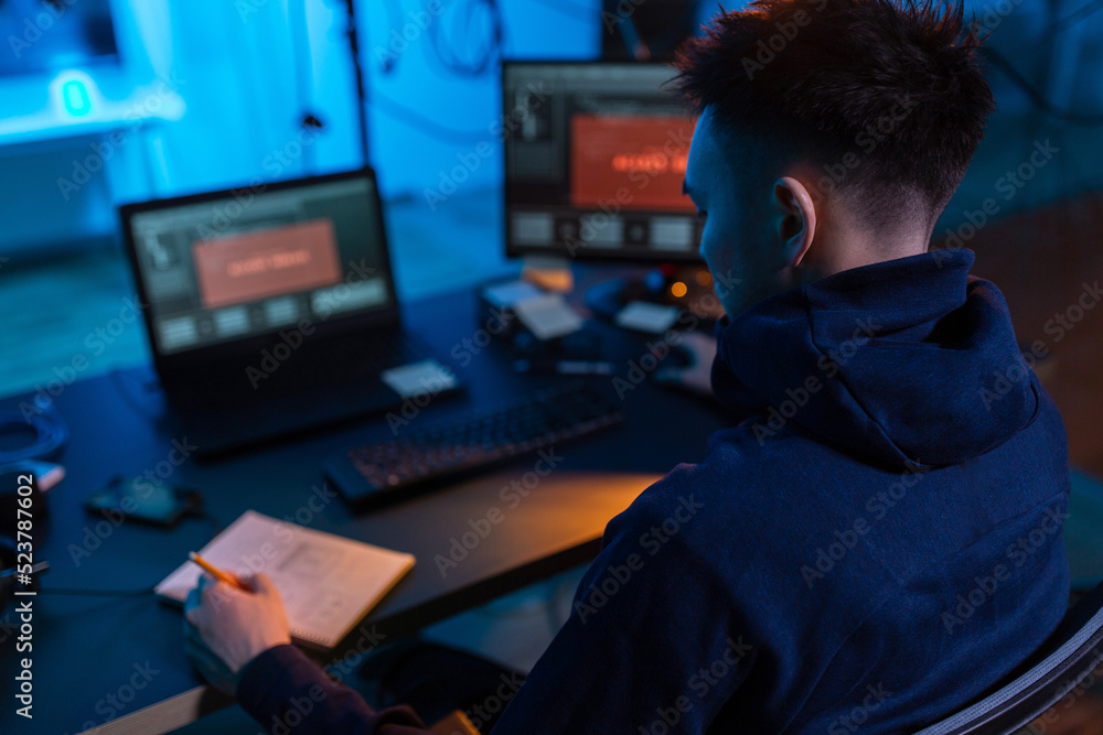 Poster cybercrime, hacking and technology concept - close up of male hacker in dark room writing to noteboo
