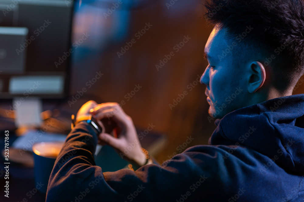 Poster cybercrime, hacking and technology concept - close up of male hacker in dark room with smart watch a