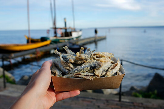 hand holding small fried fish at an seaside restaurant