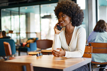 Smiling young african woman talking on cellphone at cafe