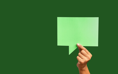 Close-up of hand holding a green speech bubble against a green background