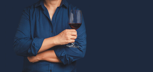 Close-up of hand holding a red wine glass while standing on a blue background