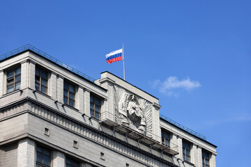 Parliament building in Moscow with Russian flag on background of blue sky. Facade of State Duma of...
