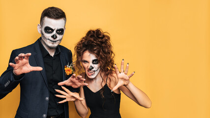 A Halloween couple in fancy dress with professional makeup poses together on a bright yellow...